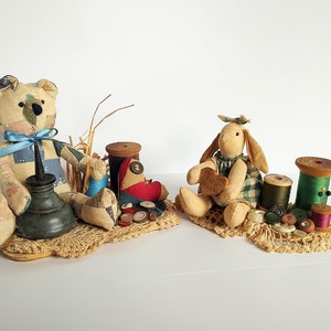 May include: Two handmade patchwork toys, a bear and a bunny, are surrounded by vintage sewing supplies, including spools of thread, buttons, and a small oil can. The bunny is holding a heart-shaped tag that reads "You Are My Sunshine".