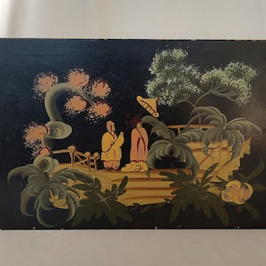 May include: A rectangular black wooden box featuring a hand-painted scene of two figures in yellow and pink robes standing on a bridge. The illustration includes green foliage, stylized trees, and a small yellow umbrella against a dark background.