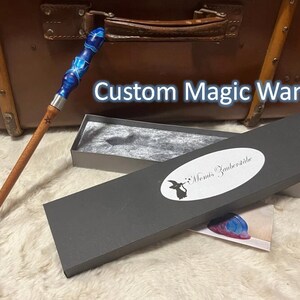 Pode incluir: Uma varinha m&aacute;gica personalizada com um cabo de resina azul e branco e um eixo de madeira. A varinha est&aacute; em uma caixa cinza com o texto "Monis Zauberstabe".