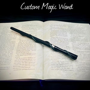 Pode incluir: Uma varinha m&aacute;gica preta e verde com um design retorcido em forma de videira. A varinha est&aacute; apoiada em um livro aberto com texto em alem&atilde;o. O t&iacute;tulo do livro &eacute; "Custom Magic Wand".