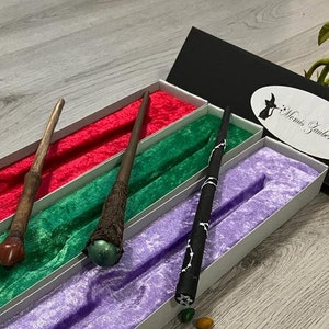 Pode incluir: Tr&ecirc;s varinhas de madeira com pontas de diferentes cores s&atilde;o exibidas em uma caixa forrada de veludo. A caixa &eacute; preta com um r&oacute;tulo branco que diz "Mami's Zauberstube".