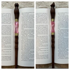 Pode incluir: Um close-up de uma varinha rosa e dourada com uma pega de madeira castanho. A varinha &eacute; feita de resina e tem um design detalhado. A varinha &eacute; um acess&oacute;rio popular para os f&atilde;s da s&eacute;rie Harry Potter.