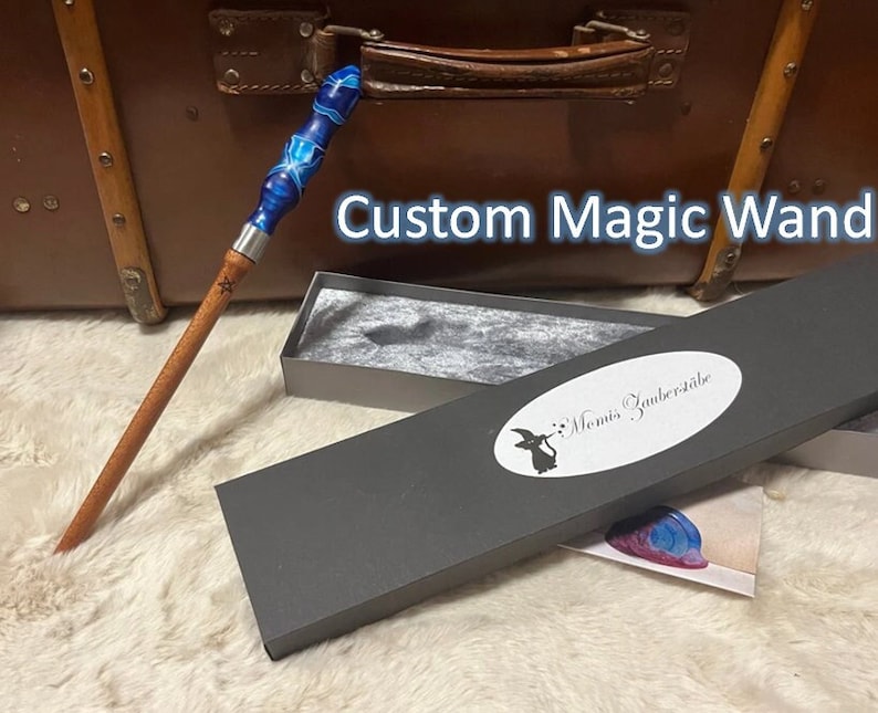 Pode incluir: Uma varinha m&aacute;gica personalizada com um cabo de resina azul e branco e um eixo de madeira. A varinha est&aacute; em uma caixa cinza com o texto "Monis Zauberstabe".