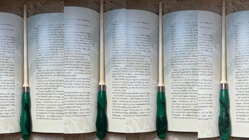 Pode incluir: Um close-up de um livro com um marcador de p&aacute;gina de madeira. O marcador &eacute; verde e branco com um design detalhado. O livro est&aacute; aberto em uma p&aacute;gina com texto em alem&atilde;o.