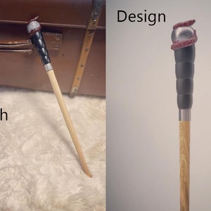Pode incluir: Uma varinha de madeira com uma al&ccedil;a preta e prateada e uma ponta vermelha e prateada. A varinha est&aacute; sobre uma superf&iacute;cie branca e fofa. As palavras "Design" e "Acabamento" est&atilde;o escritas na imagem.