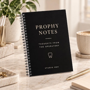 May include: A black spiral-bound notebook with the text PROPHY NOTES, THOUGHTS FROM THE OPERATORY, and STUDIO RDH printed in gold, featuring a small gold tooth icon centered on the cover. The notebook has a matte finish and white wire binding.