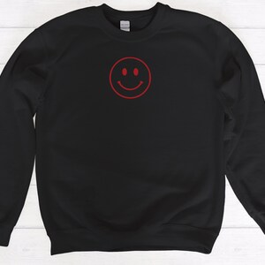 May include: Black sweatshirt with a red smiley face graphic.