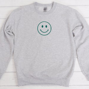 May include: A gray sweatshirt with a green smiley face graphic on the front.