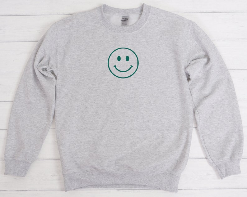 May include: A gray sweatshirt with a green smiley face graphic on the front.