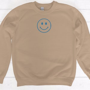 May include: A tan sweatshirt with a blue smiley face embroidered on the front.