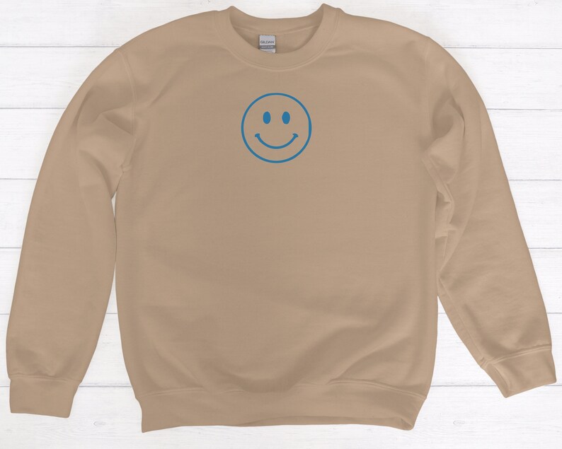 May include: A tan sweatshirt with a blue smiley face embroidered on the front.