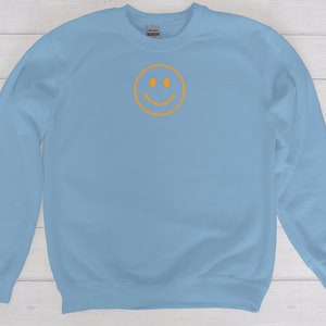 May include: A light blue sweatshirt with a yellow smiley face graphic on the front.