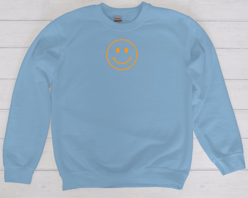 May include: A light blue sweatshirt with a yellow smiley face graphic on the front.