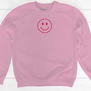 May include: A pink sweatshirt with a red smiley face graphic.