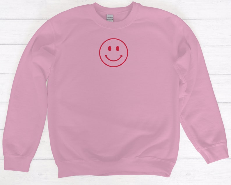 May include: A pink sweatshirt with a red smiley face graphic.