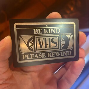 Tarjeta metálica grabada con láser "Sé amable, por favor rebobina". Recuerdo nostálgico de cinta VHS retro. Idea de regalo de aluminio anodizado para cine o sala de cine.