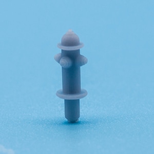May include: A small, gray plastic fire hydrant model. The hydrant has a rounded top and a cylindrical body with two small, round handles on each side.