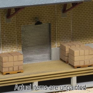 May include: A set of two wooden pallets stacked with cardboard boxes. The pallets are in front of a brick wall with a closed metal garage door. The text "Actual items are unpainted" is at the bottom of the image.