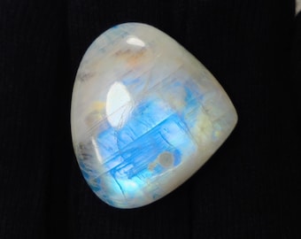 May include: A polished, teardrop-shaped moonstone with a pearlescent sheen. The stone features internal blue and white color play, with hints of yellow. The surface is smooth and reflective, set against a dark background.