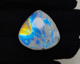 May include: A pear-shaped, iridescent moonstone gemstone. The stone displays a play of color with hues of blue, yellow, and white. The gemstone is set against a black background.