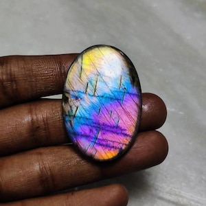 Pode incluir: Gemstone de labradorita oval com cores iridescentes azuis, roxas e amarelas. A pedra tem uma superfície lisa e polida.