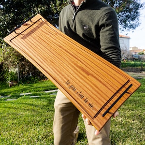 Könnte beinhalten: Ein langes, rechteckiges Holztablett mit schwarzen Metallgriffen. Das Tablett hat eine natürliche Holzmaserung und ist mit dem Text "Le gras c'est la vie..." graviert.