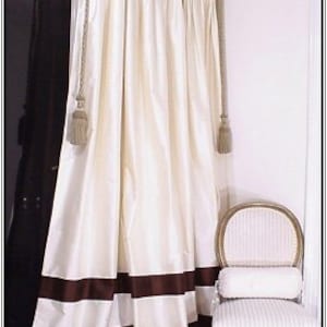 May include: White curtains with brown and white stripes at the bottom. The curtains are hung from a decorative rod and have tassels.