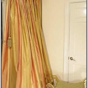 May include: Elegant, floor-length curtains with vertical stripes in peach and gold hues. The curtains are draped and hung from a decorative rod. A gold-framed bench with a green cushion sits nearby, adding to the room's luxurious feel.