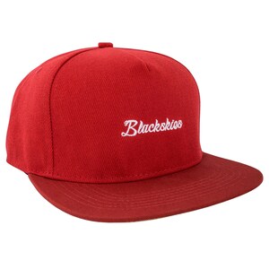Può includere: Un cappellino da baseball rosso con visiera piatta. Il cappellino presenta la scritta bianca "Blackskies" sul davanti. Il cappello è realizzato in tessuto strutturato e ha una corona strutturata.