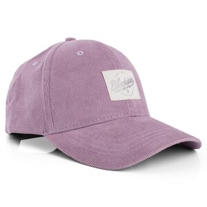 Op de afbeelding: Een lavendelkleurige corduroy baseballcap met een gebogen klep. De cap heeft een vierkante patch met de tekst "Blockskies" in een gestileerd lettertype. De hoed is gemaakt van een geribbelde stof en heeft een kleine knoop aan de bovenkant.