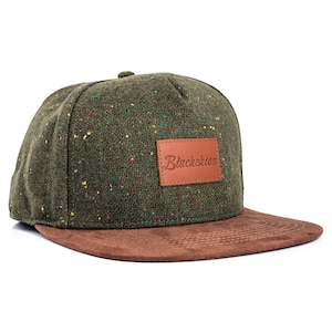May include: A green and brown baseball cap with a flat peak. The cap features a speckled, textured fabric in green, red, and yellow. A brown leather patch with the text "Blackskies" is on the front.