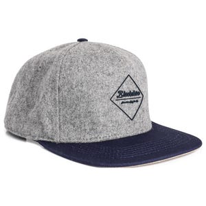 Könnte beinhalten: Graue und marineblaue Baseballkappe. Die Kappe hat eine graue Krone und einen marineblauen Schirm. Ein schwarzes rautenförmiges Logo mit dem Text "Blackblue" befindet sich auf der Vorderseite. Die Kappe hat einen flachen Schirm und einen kleinen marineblauen Knopf oben.