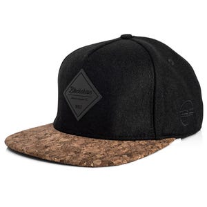Könnte beinhalten: Schwarze Baseballkappe mit Korkschirm. Die Kappe hat einen rautenförmigen Aufnäher mit dem Text "Blackskies" und "MMIX". Ein kleines Logo befindet sich an der Seite.