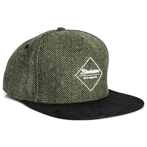 Könnte beinhalten: Grüne und schwarze Baseballkappe mit Fischgrätenmuster auf der Krone und einem flachen schwarzen Schirm. Die Kappe hat ein weißes rautenförmiges Logo mit Text.