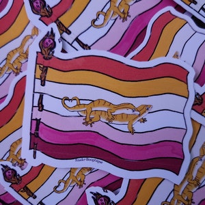 May include: Multiple stickers featuring a lesbian pride flag with two geckos on top of each other. The flag has stripes of red, orange, yellow, white, pink, and maroon. The text "Snake Booptque" is printed on the bottom of the sticker.