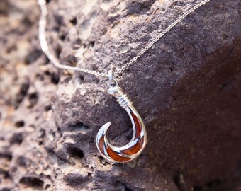 May include: A silver chain necklace with a wooden hook pendant. The hook is made of brown wood with a silver inlay. The hook is a traditional Hawaiian design.