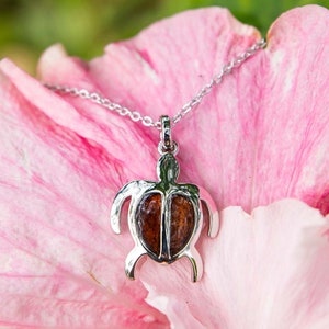 Op de afbeelding: Een zilveren ketting met een schildpad hanger gemaakt van koa hout. De schildpad is een symbool van geluk en bescherming in de Hawaïaanse cultuur.