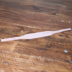 Peut inclure: Une sangle en cuir rose p&acirc;le dot&eacute;e d'une section centrale plus large qui s'effile vers les deux extr&eacute;mit&eacute;s. Une extr&eacute;mit&eacute; de la sangle comprend une fente allong&eacute;e, tandis que l'autre pr&eacute;sente une s&eacute;rie de quatre petits trous circulaires.