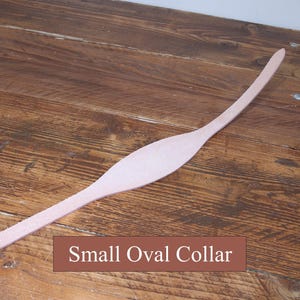 Peut inclure: Une bande de cuir beige clair allong&eacute;e pr&eacute;sentant une section centrale ovale, lisse et plus large, qui se r&eacute;tr&eacute;cit en deux extr&eacute;mit&eacute;s fines et incurv&eacute;es. Une &eacute;tiquette rectangulaire marron avec du texte blanc indique Small Oval Collar.