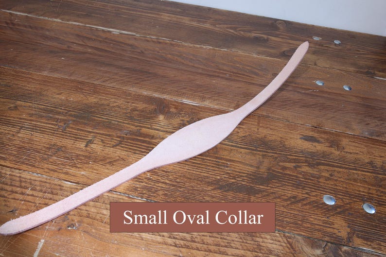 Peut inclure: Une bande de cuir beige clair allong&eacute;e pr&eacute;sentant une section centrale ovale, lisse et plus large, qui se r&eacute;tr&eacute;cit en deux extr&eacute;mit&eacute;s fines et incurv&eacute;es. Une &eacute;tiquette rectangulaire marron avec du texte blanc indique Small Oval Collar.