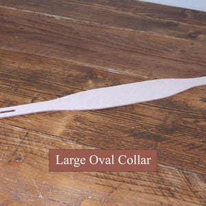 Peut inclure: Un collier en cuir beige clair dot&eacute; d'une large section centrale ovale allong&eacute;e qui s'effile vers les extr&eacute;mit&eacute;s. Une extr&eacute;mit&eacute; comprend une fente rectangulaire unique, tandis que l'autre pr&eacute;sente une s&eacute;rie de petits trous de r&eacute;glage. Texte : Large Oval Collar.