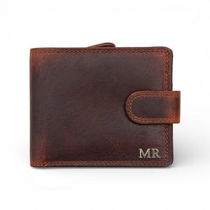 Może przedstawiać: Brązowy skórzany portfel z zapięciem na zatrzask. Portfel ma teksturowaną powierzchnię i jest wytłoczony inicjałami "MR" w kolorze srebrnym. Krawędzie są przeszyte kontrastującą nicią.