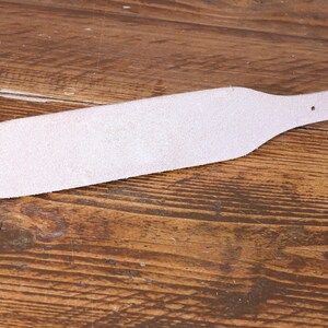 Peut inclure: Une sangle en cuir rose clair avec une section centrale large et effil&eacute;e et une extr&eacute;mit&eacute; &eacute;troite comportant une s&eacute;rie de trous de r&eacute;glage circulaires r&eacute;guli&egrave;rement espac&eacute;s. La sangle pr&eacute;sente une surface textur&eacute;e et un bord lisse.