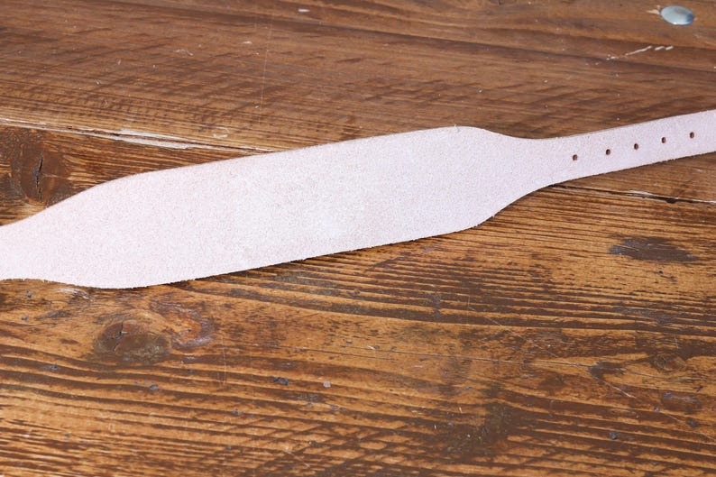 Peut inclure: Une sangle en cuir rose clair avec une section centrale large et effil&eacute;e et une extr&eacute;mit&eacute; &eacute;troite comportant une s&eacute;rie de trous de r&eacute;glage circulaires r&eacute;guli&egrave;rement espac&eacute;s. La sangle pr&eacute;sente une surface textur&eacute;e et un bord lisse.