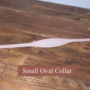 Peut inclure: Une pi&egrave;ce de cuir lisse, allong&eacute;e et de couleur beige clair, dot&eacute;e d'une section centrale ovale plus large et d'extr&eacute;mit&eacute;s effil&eacute;es, avec le texte "Small Oval Collar" imprim&eacute; en blanc sur un fond rectangulaire marron sous l'objet.
