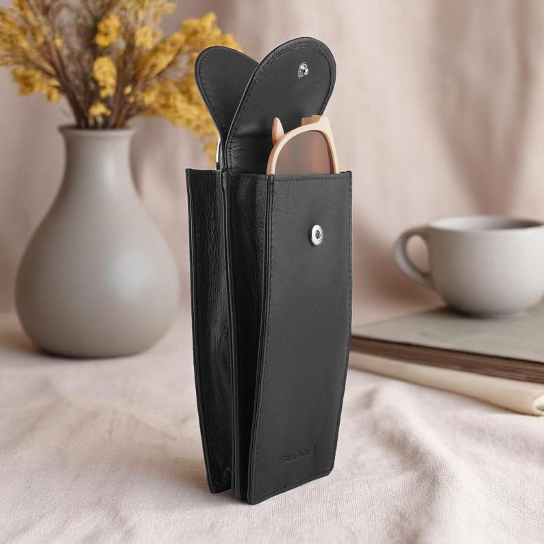 Black leather glasses case with a flap that opens to reveal a pair of glasses inside.