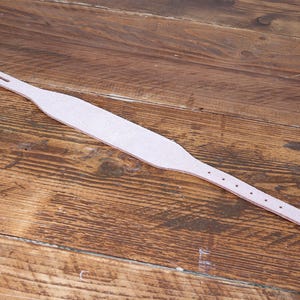 Peut inclure: Une sangle en cuir beige clair dot&eacute;e d'une section centrale plus large qui s'effile vers les deux extr&eacute;mit&eacute;s. Une extr&eacute;mit&eacute; comporte une fente rectangulaire, tandis que l'autre pr&eacute;sente une s&eacute;rie de cinq trous circulaires espac&eacute;s.