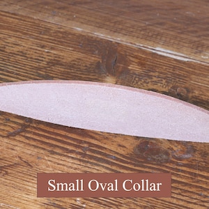 Peut inclure: Une bande de cuir rose clair incurv&eacute;e avec une texture lisse, positionn&eacute;e horizontalement. Sous la bande, une &eacute;tiquette rectangulaire marron pr&eacute;sente le texte blanc Small Oval Collar, identifiant l'objet comme un petit collier ovale.