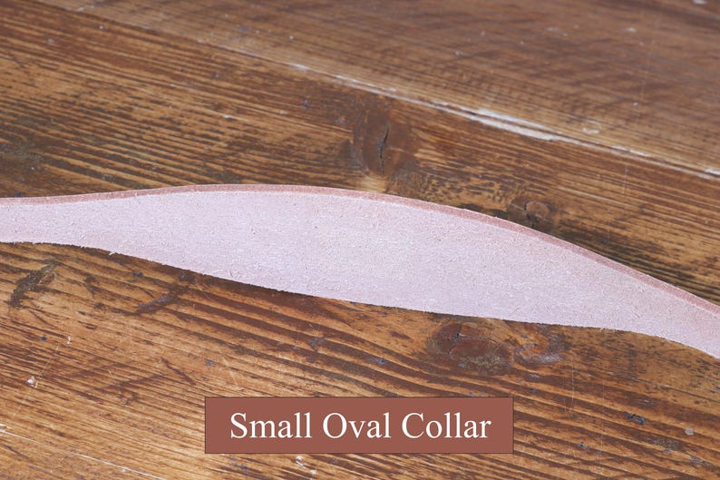 Peut inclure: Une bande de cuir rose clair incurv&eacute;e avec une texture lisse, positionn&eacute;e horizontalement. Sous la bande, une &eacute;tiquette rectangulaire marron pr&eacute;sente le texte blanc Small Oval Collar, identifiant l'objet comme un petit collier ovale.
