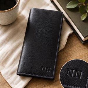 May include: A rectangular black leather wallet with a textured surface and visible stitching along the edges. The bottom right corner features the embossed letters NN in a serif font. The wallet is tall and slim, designed for vertical storage.